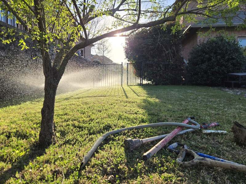 Sprinklers watering a Parker County backyard lawn with irrigation repair tools in the grass after an Abiding Irrigation Repair job