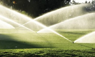Lawn sprinklers spraying arcs of water across a green lawn